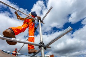 A building site worker wearing a harness walks across scaffolding