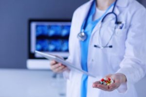 A doctor holding a tablet device in one hand and medication pills in the other hand