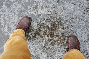 A person wearing yellow trousers and brown boots standing on an icy path.