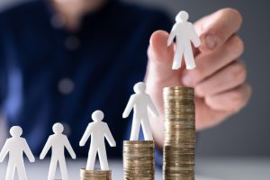 Towers of coins, growing in size from left to right, each with a white plastic figure of a person on top.