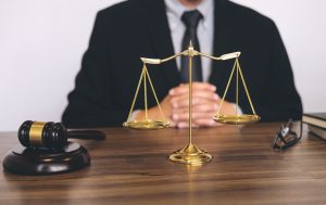 A solicitor in a suit sits behind a desk and a set of scales, explaining how to claim compensation.