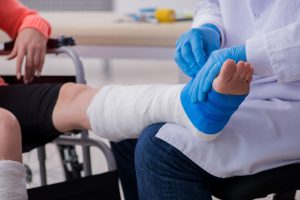 A doctor putting a cast on the leg of a man in a wheelchair.