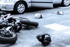 A car and motorcycle accident scene with a helmet in the foreground. 