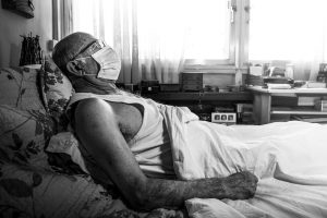 An elderly male lung cancer patient is in a hospital bed