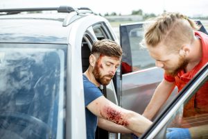 Man with injured elbow following a car accident with another man helping him