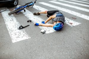 A cyclist lays on the road on a pedestrian crossing in front of a car. 