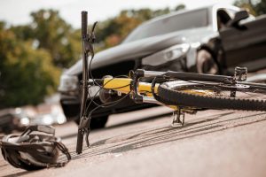 A bicycle and helmet lay on the road in front of a car. 