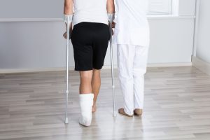Man with crutches is helped by a physical therapist to walk 